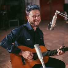 Scheuer smiling playing guitar.